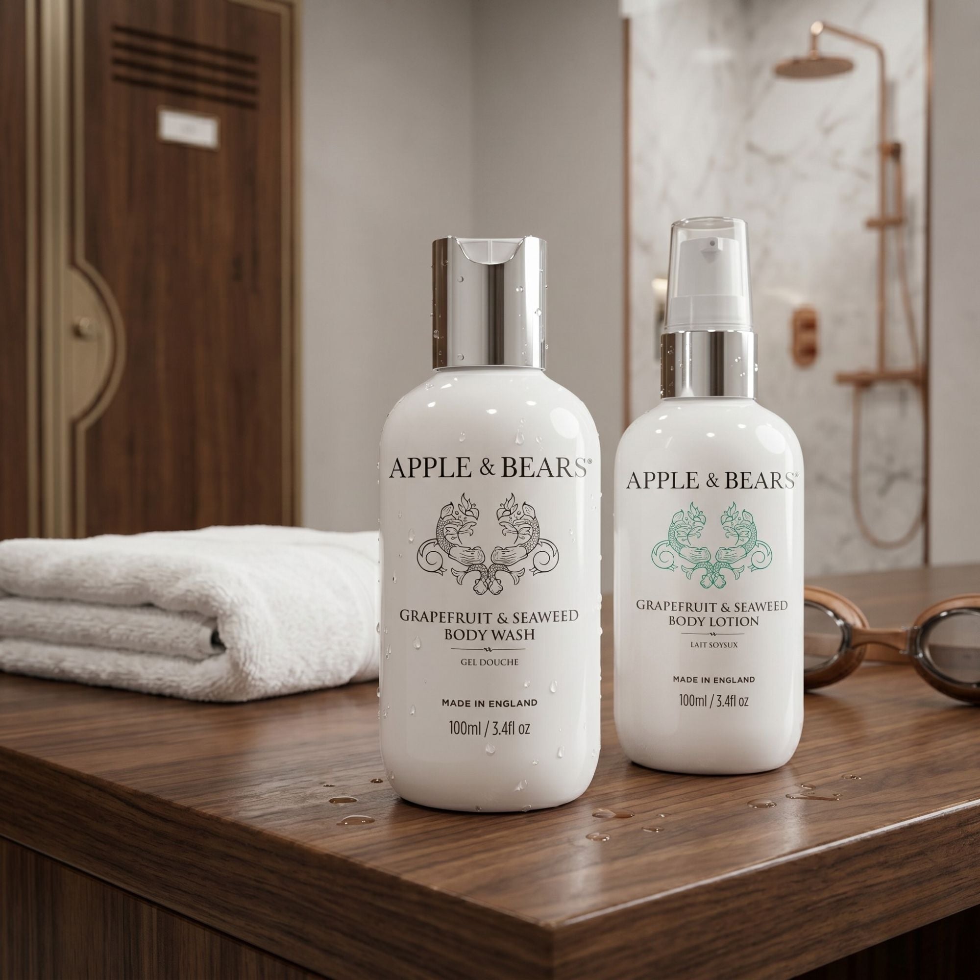 Apple & Bears Grapefruit and Seaweed Body Wash and Body Lotion 100ml with water droplets on wooden poolside bench beside swimming goggles and white towel in luxury spa shower room