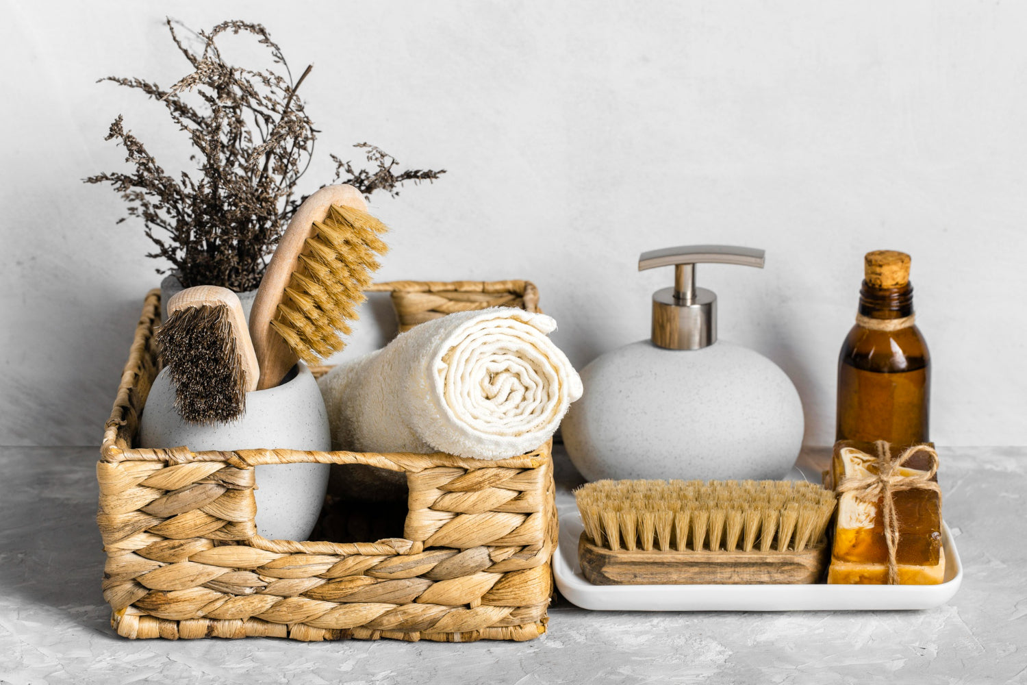 A natural wicker basket filled with zero-waste eco-friendly wooden bath brushes, a rolled white towel, organic soap bars, and sustainable bathroom accessories.