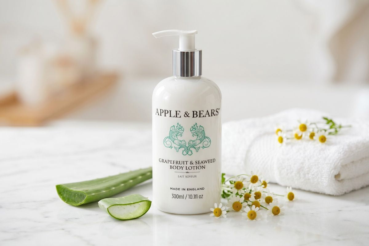 Apple and Bears Grapefruit and Seaweed Body Lotion 300ml on a white marble surface with fresh aloe vera, chamomile flowers, and white towels — gentle natural skincare made in England
