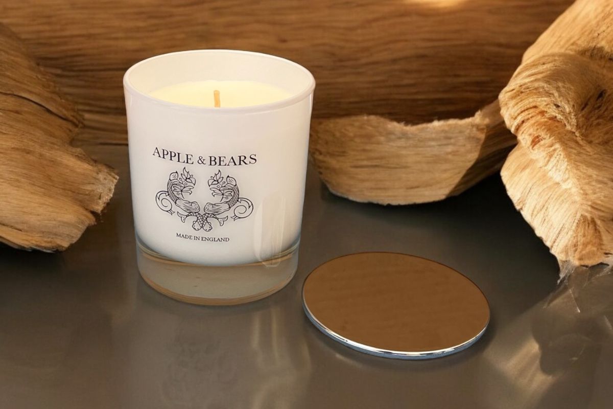 Apple & Bears Sandalwood & Black Pepper natural soy wax candle made in England, styled on driftwood with a warm lit flame — premium home fragrance for autumn and winter