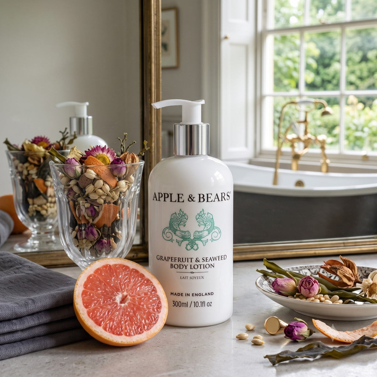 Apple & Bears Grapefruit & Seaweed Body Lotion 300ml on a marble bathroom counter with fresh grapefruit, dried botanicals and a gold bath tap — natural vegan body lotion made in England