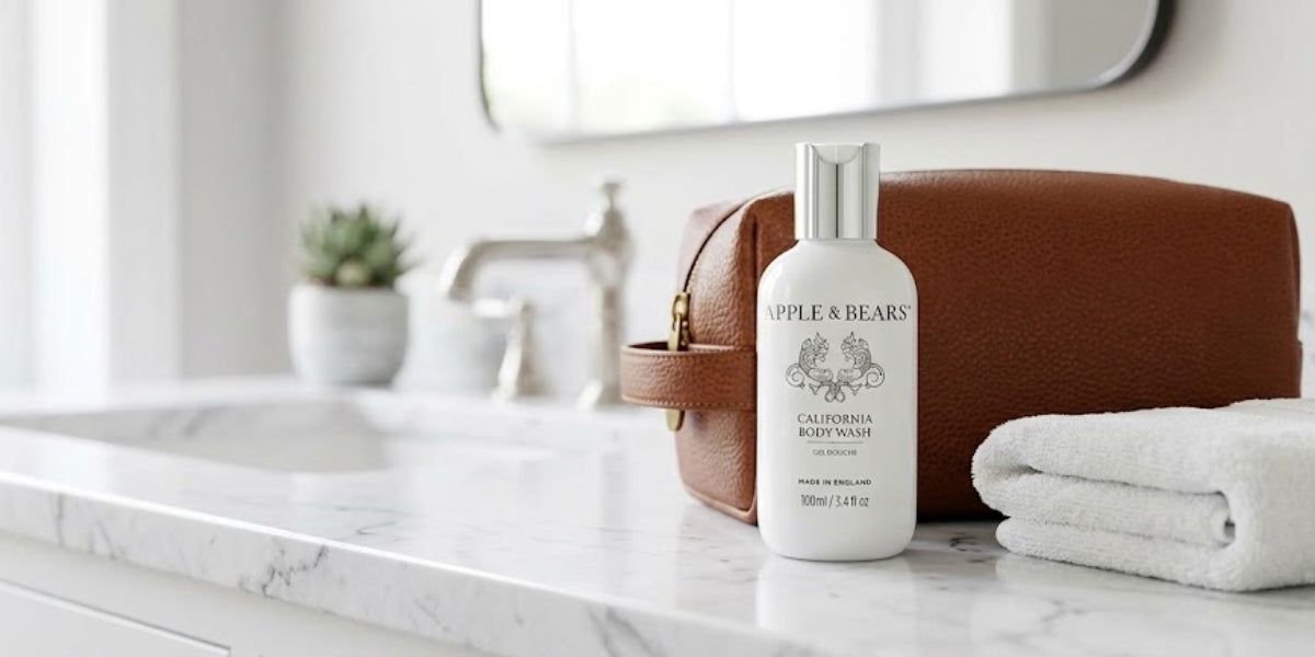 APPLE & BEARS California Body Wash 100ml travel bottle on a marble bathroom counter beside a tan leather toiletry bag and folded white towel