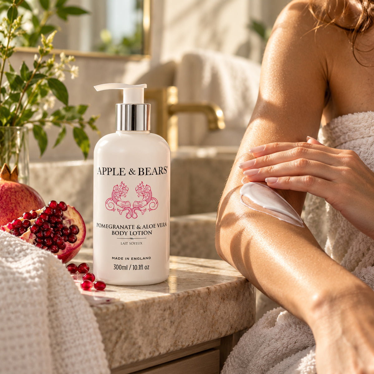 APPLE &amp; BEARS Pomegranate &amp; Aloe Vera Body Lotion 300ml beside fresh pomegranate while a woman applies body lotion to her arm in a warm bathroom setting.