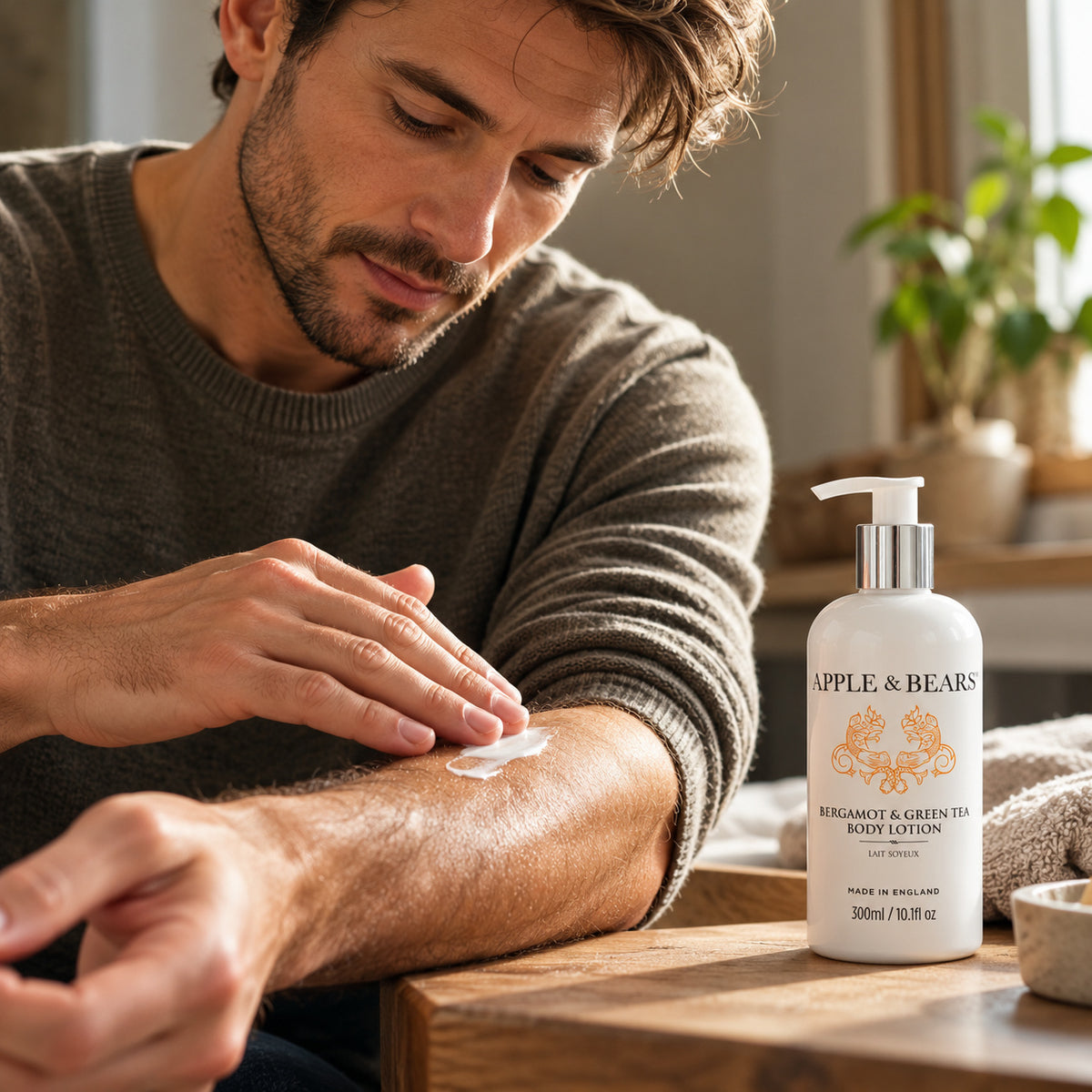 Man applying APPLE &amp; BEARS Bergamot &amp; Green Tea Body Lotion 300ml to his forearm, with the moisturiser bottle displayed on a wooden table.