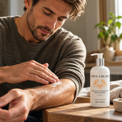 Man applying APPLE &amp; BEARS Bergamot &amp; Green Tea Body Lotion 300ml to his forearm, with the moisturiser bottle displayed on a wooden table.