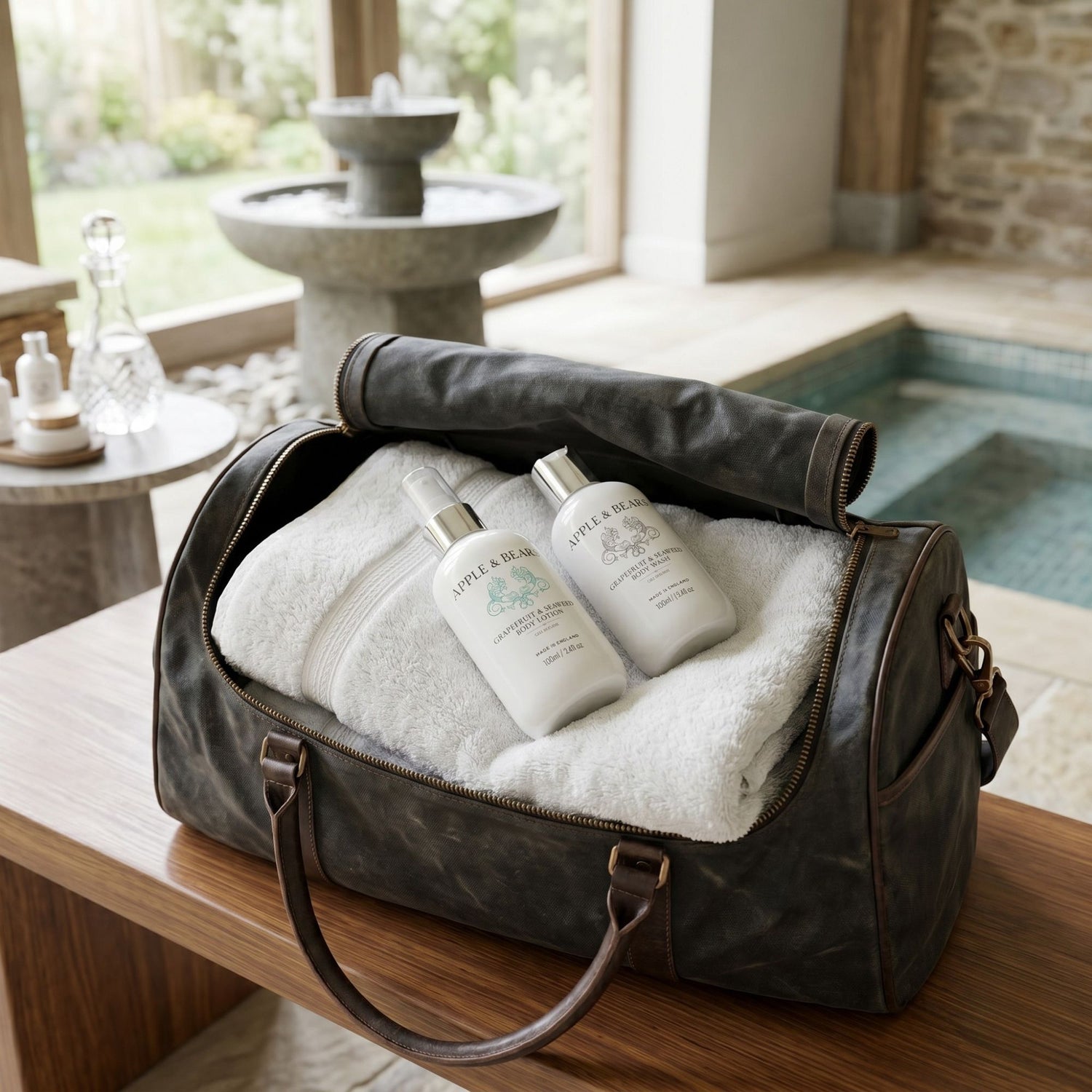 Apple &amp; Bears Grapefruit and Seaweed Body Lotion and Body Wash 100ml nestled in white towels inside a luxury leather holdall beside a private spa pool with stone fountain