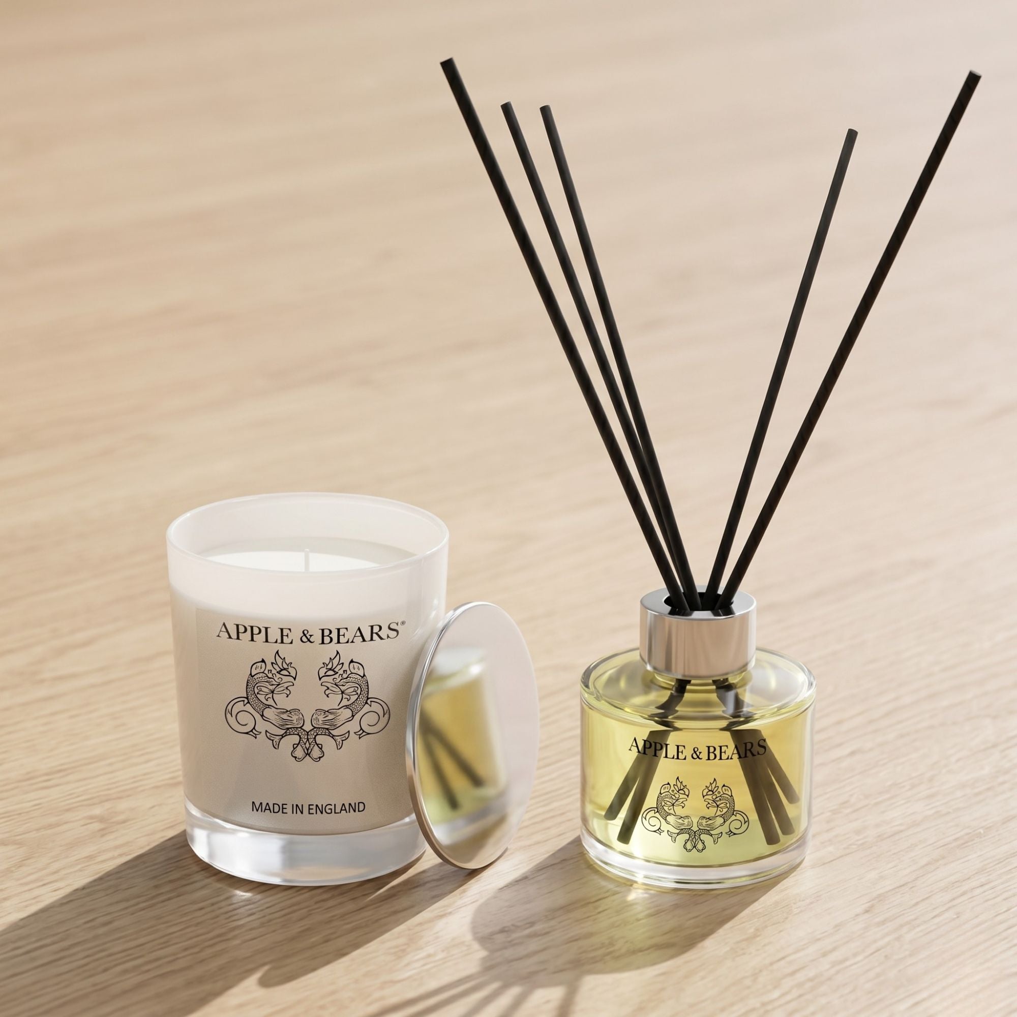 Lifestyle view of the Apple &amp; Bears Lavender Sleep Sanctuary soy wax candle and 125ml reed diffuser with black rattan reeds, displayed on a natural wooden surface with soft, warm lighting.