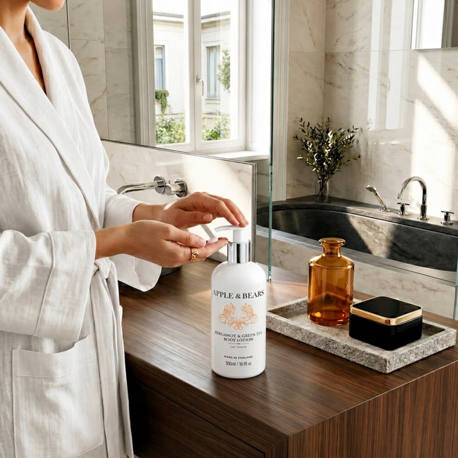 Woman in white robe pumping Apple &amp; Bears Bergamot &amp; Green Tea Body Lotion 300ml in a luxury marble bathroom