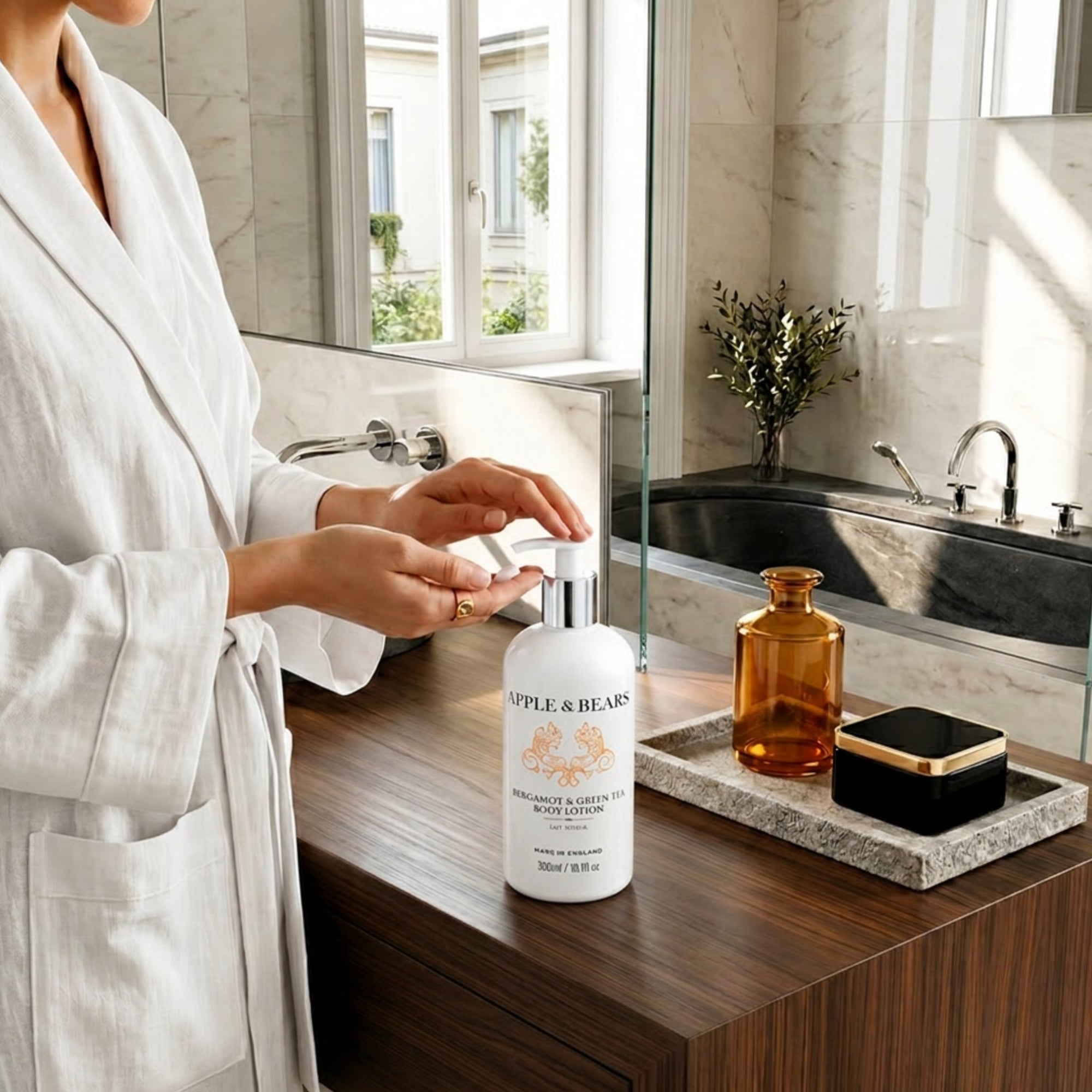 Woman in white robe pumping Apple &amp; Bears Bergamot &amp; Green Tea Body Lotion 300ml in a luxury marble bathroom