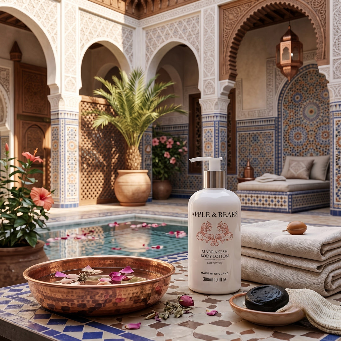 Apple &amp; Bears Marrakesh Body Lotion 300ml on mosaic tiled surface in a Moroccan riad courtyard with rose petal pool, arched doorways and copper bowl