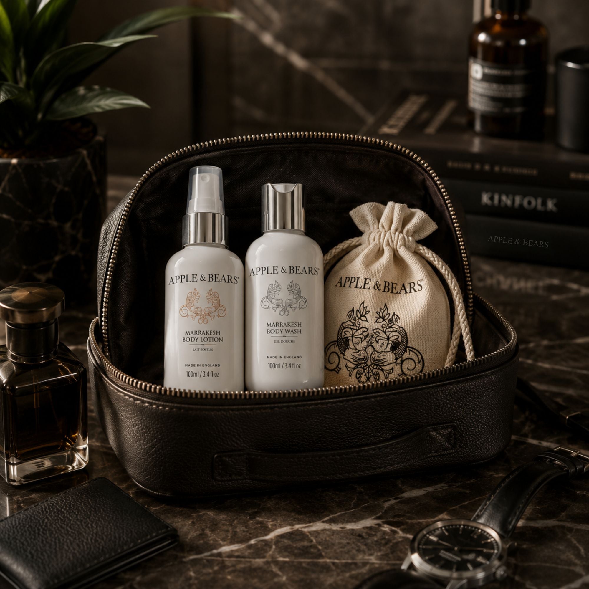Apple &amp; Bears Marrakesh Travel Gift Set 100ml/3.4 fl oz with eco cotton drawstring bag displayed in open black leather dopp kit with Kinfolk book and watch on dark marble, Made in England