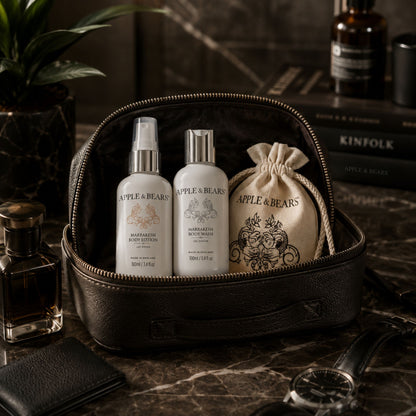 Apple &amp; Bears Marrakesh Travel Gift Set 100ml/3.4 fl oz with eco cotton drawstring bag displayed in open black leather dopp kit with Kinfolk book and watch on dark marble, Made in England